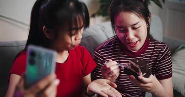 Handheld shot, Two Asian siblings sit on a sofa and use cell phone to talk to friends via call in a cozy living room. Share good times video