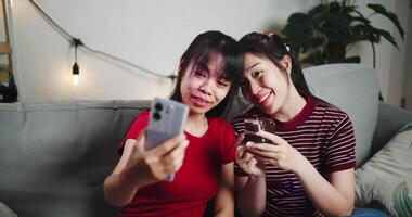 Handheld high angle view shot, Two Asian siblings sit on a sofa and use cell phone to talk to friends via call in a cozy living room. Share good times video