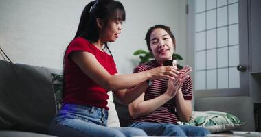 Handheld low angle view shot, The elder sister gave a small cake with candles to her younger sister and sang a happy birthday song together on the sofa in the warm room. video