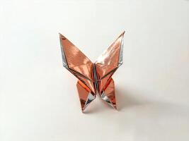 symmetrical origami butterfly crafted from shiny metallic paper in gold and silver tones featuring intricate detailed folds and a sleek modern artistic aesthetic placed on a smooth neutral surface photo