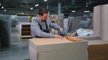 Skilled worker uses a pneumatic stapler to attach fabric to a sofa base frame video