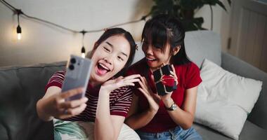 Handheld high angle view shot, Two Asian siblings pose for a selfie happily and joyfully on a sofa in their living room at home, Capture happy moments together video