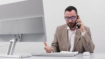 Angry business man talking on phone, looking at computer monitor, stressed frustrated office worker arguing by mobile solving online computer problem with technical support complaining on bad service video