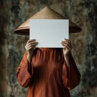 A woman wearing a brown hat and orange dress holding a white piece of paper photo