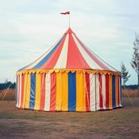 A large circus tent with a red, yellow, and blue striped canopy photo