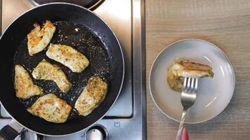 Top view of grilled chicken fillets frying in a pan next to a plate where a piece is served with a fork, showing contrast between cooking and serving stage video