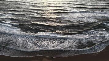 View of layered ocean waves breaking on dark wet beach with foam and sunset glow video