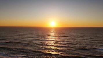 Golden sunset over calm ocean with soft waves and shimmering light, aerial view video