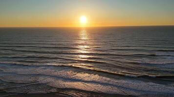 Sunset over calm ocean waves seen from drone flying above empty shoreline video