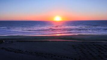 Pastel ocean sunset with beach walkers and descent behind dune at golden hour video