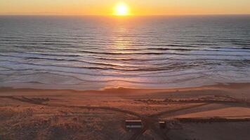 Golden sunset over ocean waves with beach structures and soft reflections video