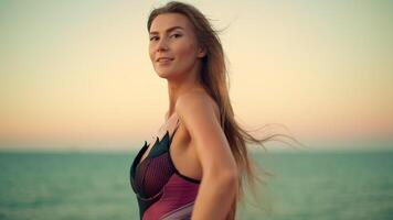 sunrise tall girl stands on beach soft breeze blowing her long hair and colorful fabric She beams joy against serene backdrop of ocean and sky video