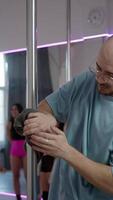 A serious-looking bald man is carefully cleaning the pole with a cloth, making it clean and smooth for dance classes in a dance studio. video
