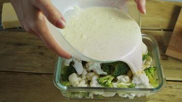 Broccoli and cauliflower are placed in a baking dish and covered with a cheese-based sauce to create a delicious casserole or gratin. video