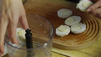 Boiled eggs are cut in half and added to an electric blender. The blender is used to grind the eggs into a homogeneous mass. video