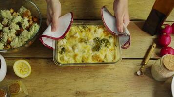 A delicious hot dish of vegetables, broccoli and potatoes, with a crispy cheese crust, is placed on a rustic wooden table. Top view. video