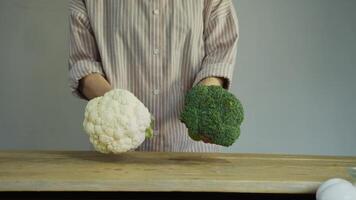The chef brings two large florets of broccoli and cauliflower to the wooden table, carefully choosing between these vegetables. video