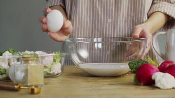 chef carefully breaks egg onto edge of bowl and pours it carefully into cream, creating delicious cheese and cream sauce for vegetable dish. video