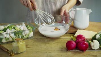 The egg yolk is whisked and mixed with a wire whisk in a creamy sauce made from milk and cheese for a vegetable casserole. video