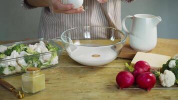 Cook breaks egg's shell on the rim of bowl and pours egg into cream. They then stir mixture to create delicious, creamy sauce that will be served with vegetables like broccoli and cauliflower. video