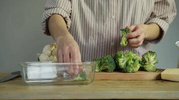 Hostess at table filled with variety of fresh, ripe vegetables, carefully cuts large heads of broccoli into smaller, convenient pieces, preparing them for cooking delicious vegetarian dish. video