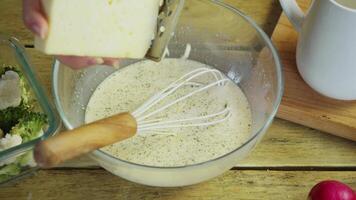 Piece of hard cheese is grated and mixed with special sauce to create delicious vegetable gratin, which is then baked in oven. video