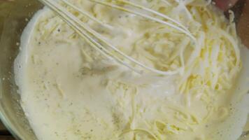 Extreme close-up of a whisk mixing grated cheese with creamy yogurt in the process of creating a delicious dairy dish. Top view. video