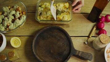 Chef uses spatula to serve portion of freshly baked, hot broccoli and cauliflower gratin, topped with cheese. Gratin is prepared in rustic kitchen, with a wooden table. video