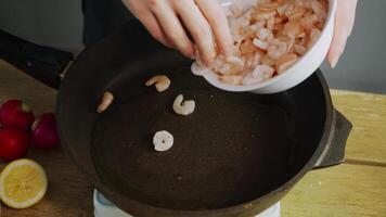 Chef lays out the frozen shrimp on a hot frying pan with oil and begins cooking them. The shrimp start to sizzle and smoke as they cook. video