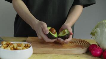 Cook cuts ripe, juicy, and colorful avocado in half during the preparation of salad or guacamole, and then removes stone from core. video
