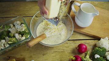 Surrounded by various vegetable ingredients, the chef grates a large piece of cheese and adds it to a creamy sauce along with broccoli and cauliflower. video