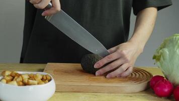 Cook is trying carefully to slice avocado, but stone is in middle of it and preventing him from doing so. He is using wooden chopping board. video