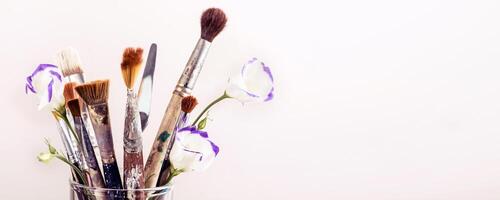 Art brushes and flowers in glass on white background. Banner format photo