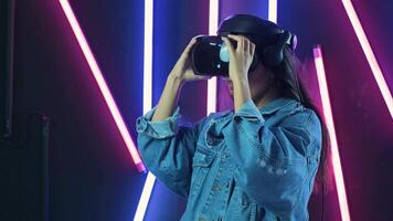 Young woman puts on vr headset, looks around and wonders how amazing in the virtual reality. Virtual reality helmet on color lighting background video