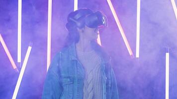 Young woman looks around and wonders how amazing in the virtual reality. Virtual reality helmet on color lighting smoke background 2 video