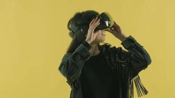 Young woman looks around and wonders how amazing in the VR world. Virtual reality helmet on the yellow background. Portrait 2 video