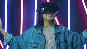 Young woman looks around and wonders how amazing in the VR headset. Virtual reality helmet on color lighting background video