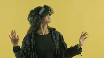 Young woman looks around and wonders how amazing in the VR headset. Virtual reality helmet on the yellow background video
