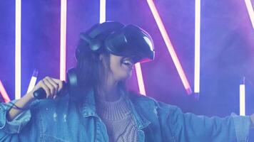 Young woman dancing in the VR headset. Virtual reality helmet on color lighting smoke background video