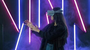Young woman playing, looks around and wonders how amazing in the VR headset. Virtual reality helmet on color lighting smoke background video