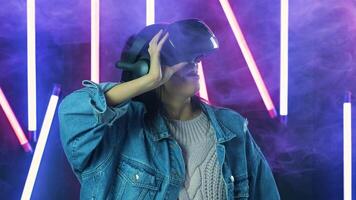 Young woman looks around and wonders how amazing in the virtual reality. Virtual reality helmet on color lighting smoke background video