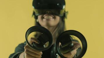Young woman playing with controllers and wonders how amazing in the VR headset. Virtual reality helmet on the yellow background. 2 video
