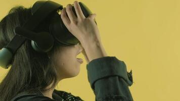 Young woman puts on vr headset, looks around and wonders how amazing in the VR world. Virtual reality helmet on the yellow background 2 video
