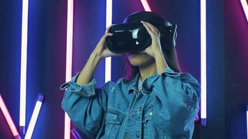 Young woman puts on VR headset and wonders how amazing in the VR world. Virtual reality helmet on color lighting background 2 video