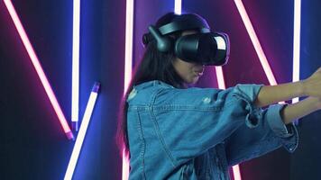 Young woman playing and smiling in the VR headset. Virtual reality helmet on color lighting background video