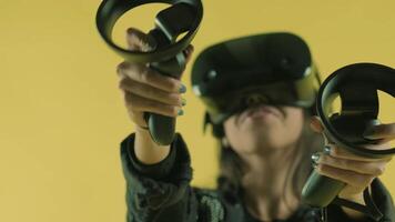 Young woman playing with controllers and wonders how amazing in the VR headset. Virtual reality helmet on the yellow background. 3 video