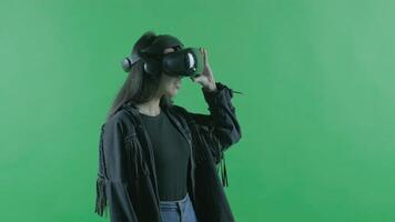 Young woman looks around and wonders how amazing in the VR headset. Virtual reality helmet on the green background. Chroma Key video