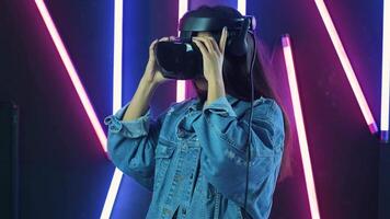 Young woman puts on vr headset, looks around and wonders how amazing in the virtual reality. Virtual reality helmet on color lighting background 2 video