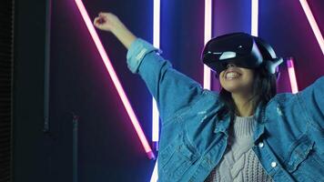 Happy young woman looks around and wonders how amazing in the VR headset. Virtual reality helmet on color lighting background video