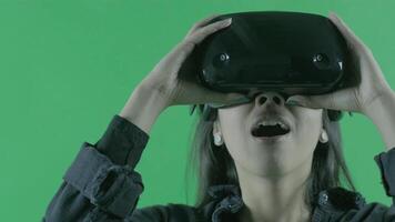 Young beautiful puts on, looks around and wonders how amazing in the VR headset. Virtual reality helmet on the green background. Chroma Key video